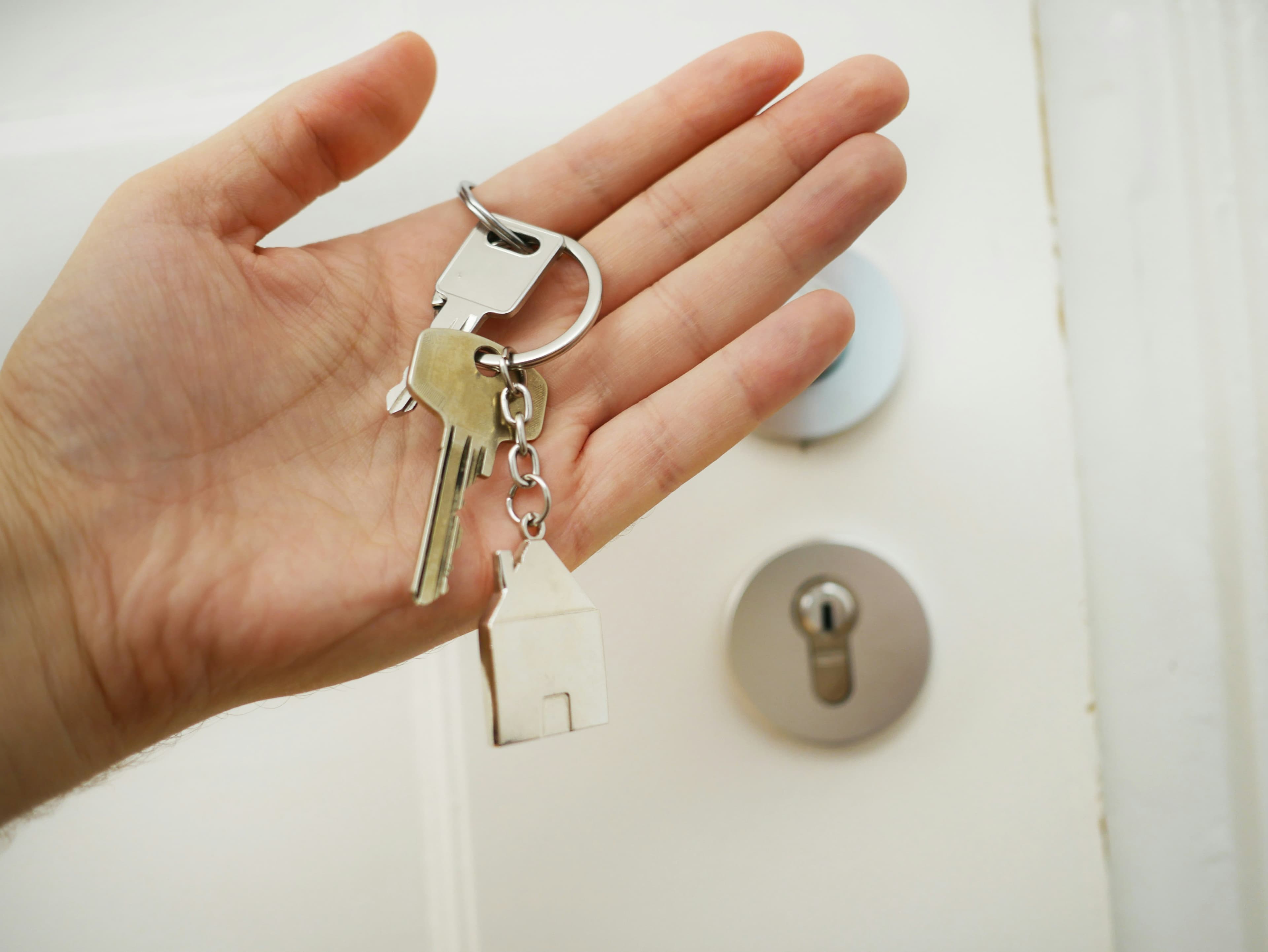 Hand holding keys in front of house front door